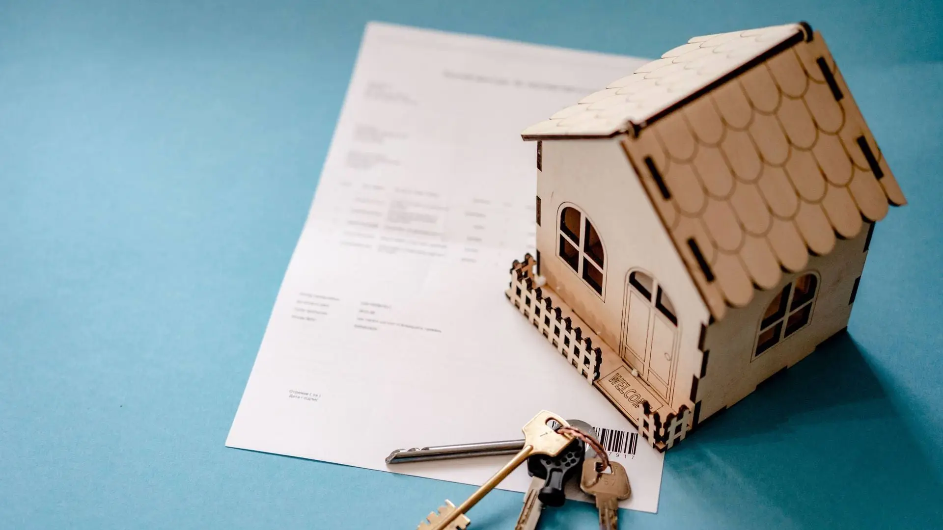 Wooden model house with a set of keys on a mortgage contract, on a teal desk