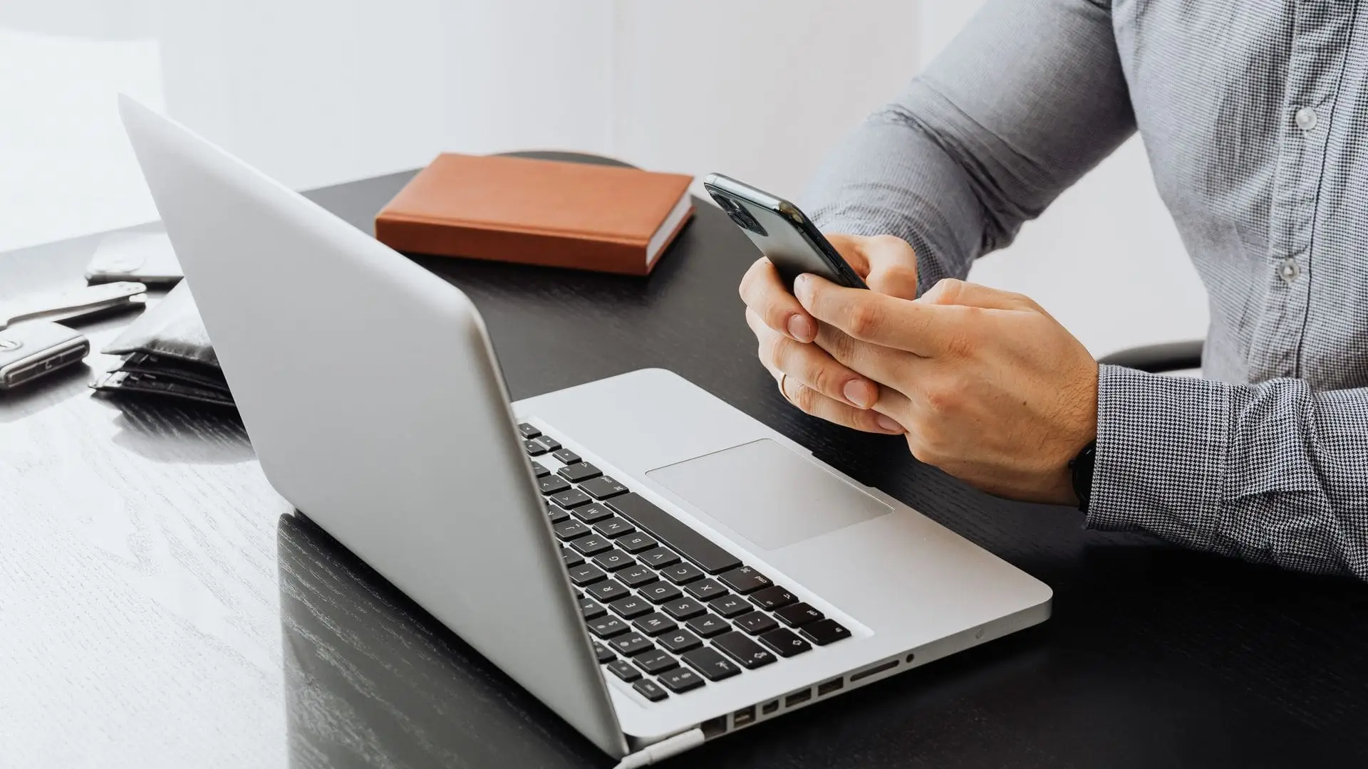 Person at an office desk confirming a sign-in on a smartphone beside an open laptop