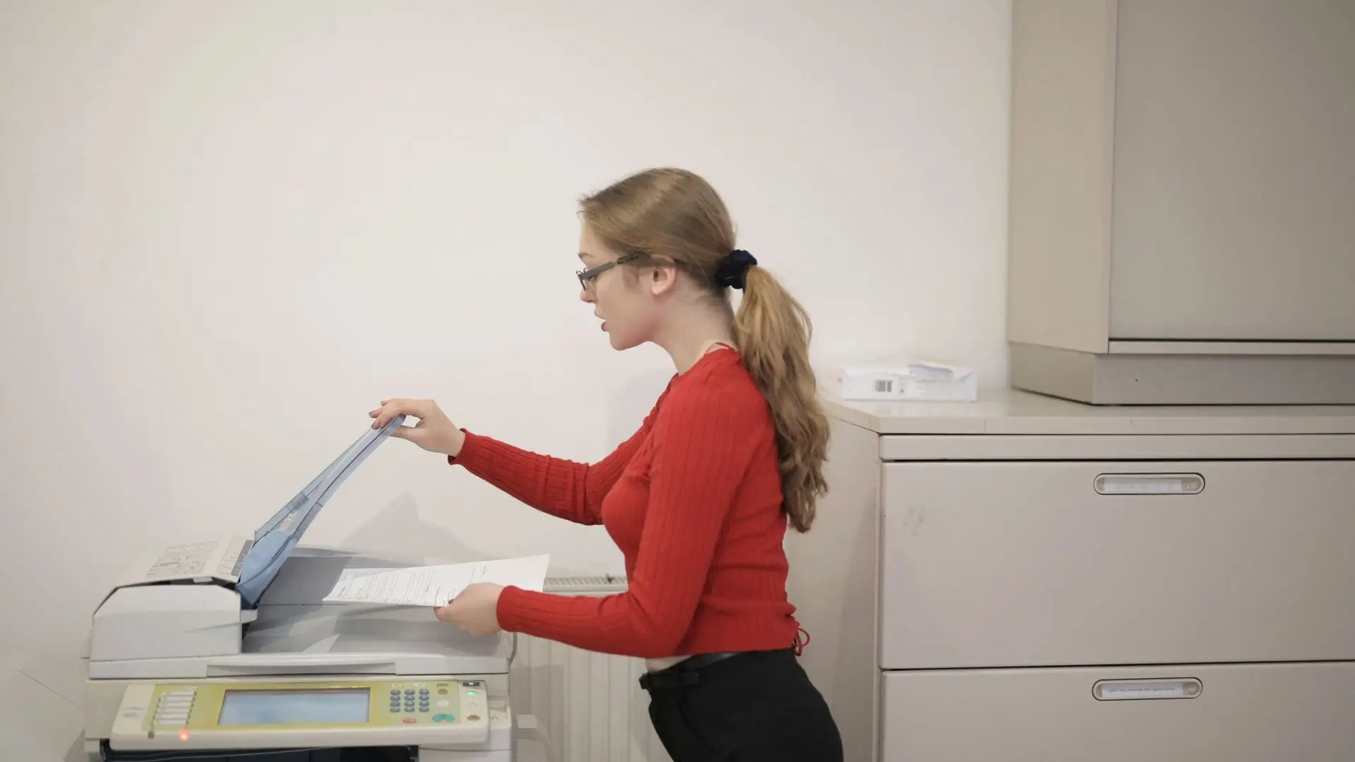 Office worker scanning documents on a multifunction printer beside filing cabinets