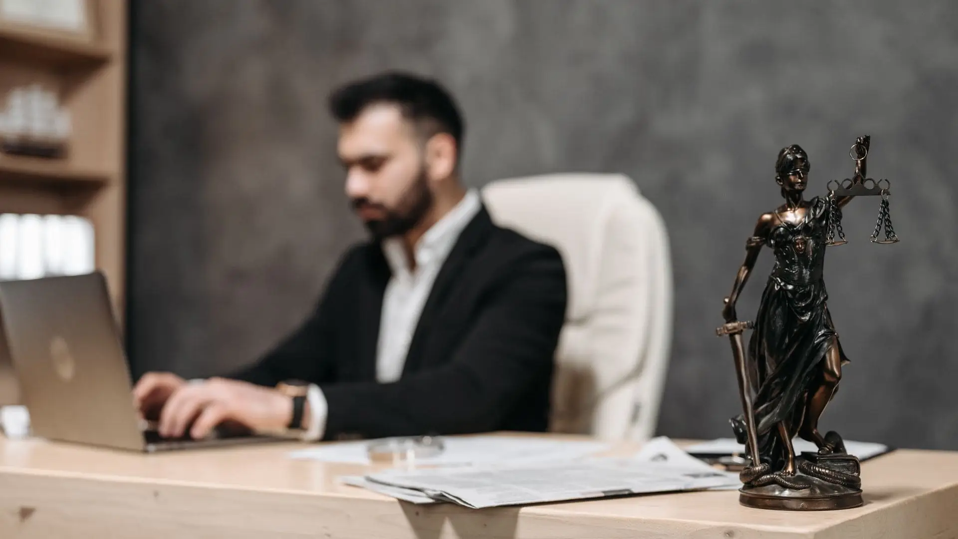 Solicitor working on a laptop at a desk in a law office, with a Lady Justice statue in the foreground