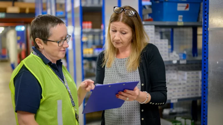 Office and stores staff at a small manufacturer checking a clipboard by stock shelving, illustrating managed IT support cost per user