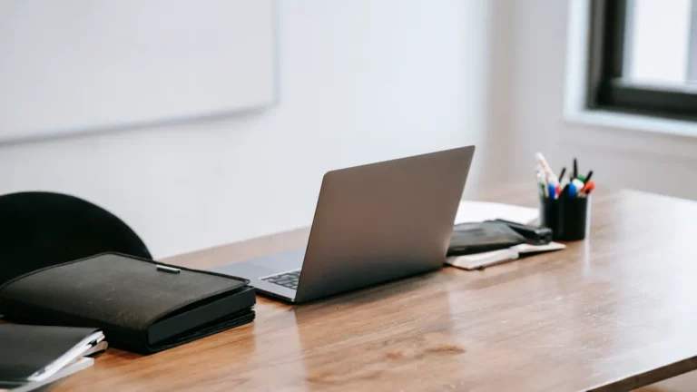 Payment redirection fraud: a laptop and document folders on a wooden desk in a quiet advisory office
