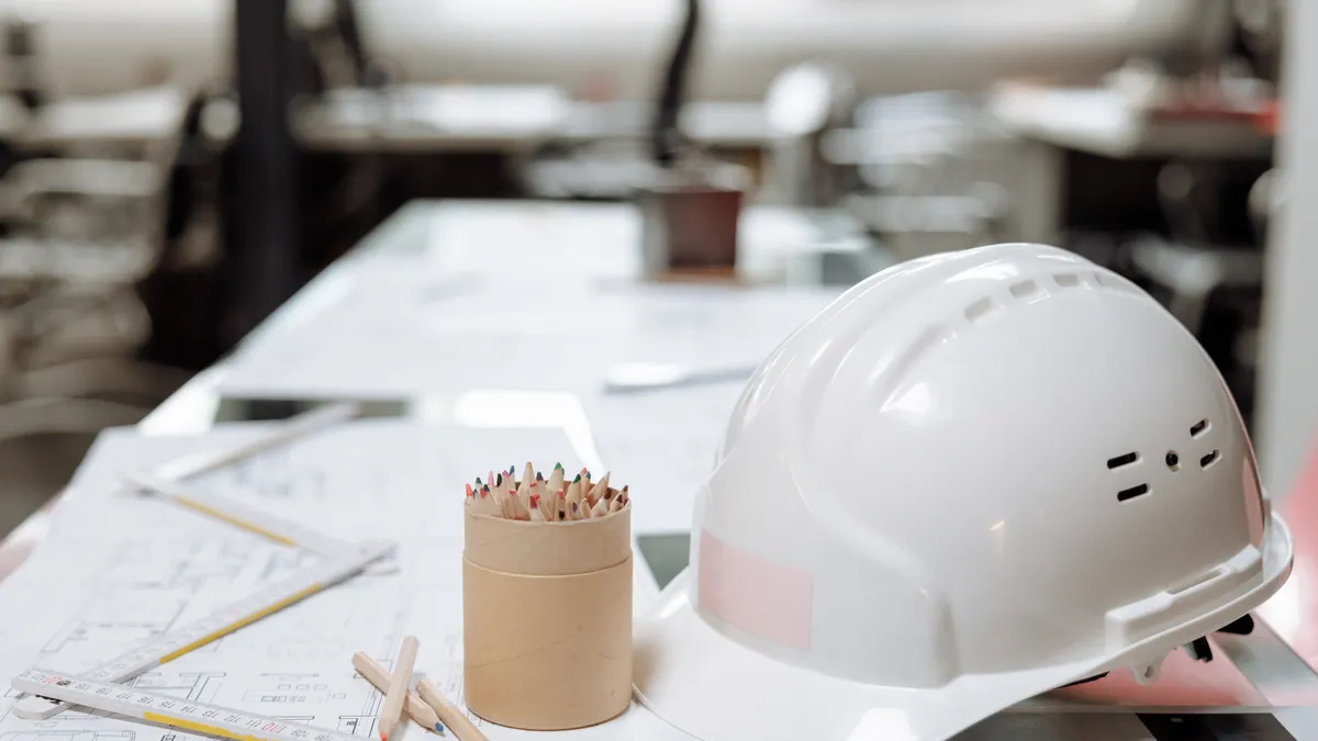 Remote access to CAD files: a white hard hat, pencils and printed drawings on a design office desk