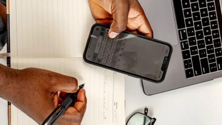 Revenue phishing emails: accountant checking a text message on a phone beside a laptop and notebook